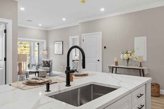 kitchen featuring crown molding, white cabinets, light stone countertops, a sink, and baseboards