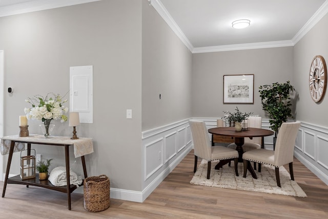 dining room with light wood-style floors, ornamental molding, and a decorative wall