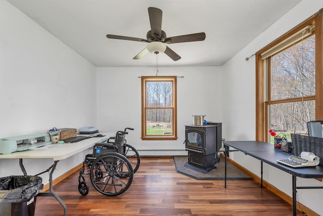 office with a wood stove, wood finished floors, baseboards, ceiling fan, and baseboard heating