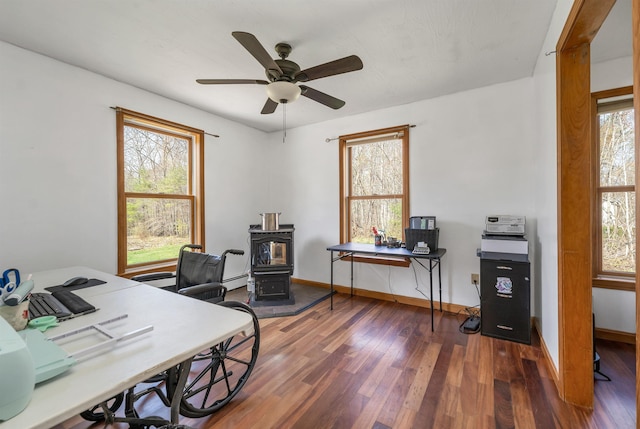 office space with baseboards, a ceiling fan, wood finished floors, and a wood stove