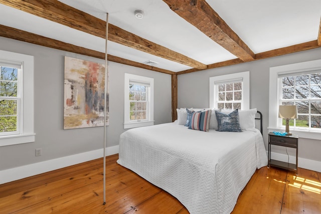 bedroom featuring baseboards, multiple windows, beam ceiling, and hardwood / wood-style floors