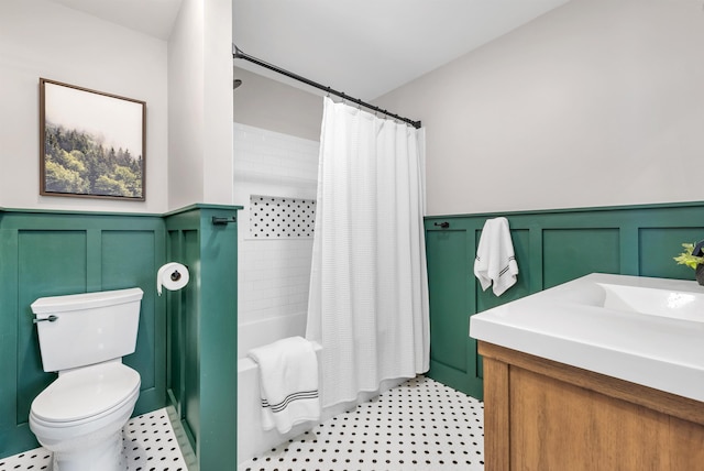 bathroom with vanity, a decorative wall, toilet, shower / bath combination with curtain, and a wainscoted wall