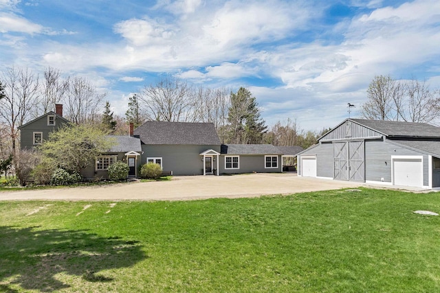 rear view of property featuring an outbuilding, a yard, a chimney, and concrete driveway
