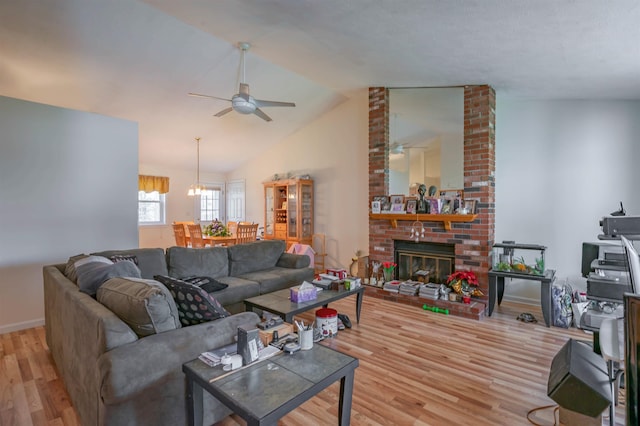 living room featuring a fireplace, vaulted ceiling, wood finished floors, baseboards, and ceiling fan with notable chandelier