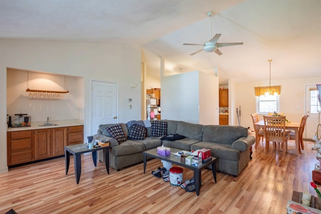 living room featuring high vaulted ceiling, ceiling fan with notable chandelier, and light wood-style floors