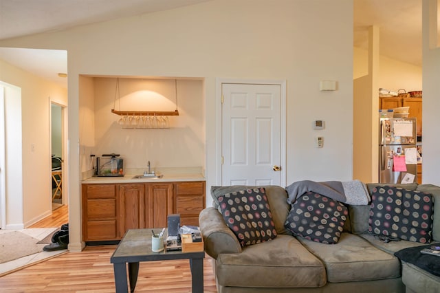 living room featuring light wood-style floors, baseboards, wet bar, and lofted ceiling