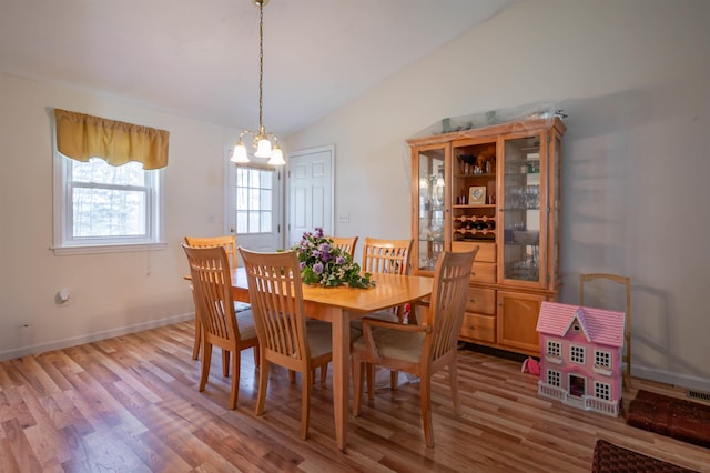 dining space with baseboards, a notable chandelier, lofted ceiling, and light wood-type flooring