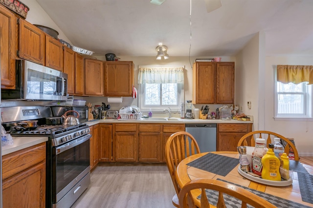 kitchen with brown cabinetry, light wood-style floors, light countertops, a sink, and stainless steel appliances