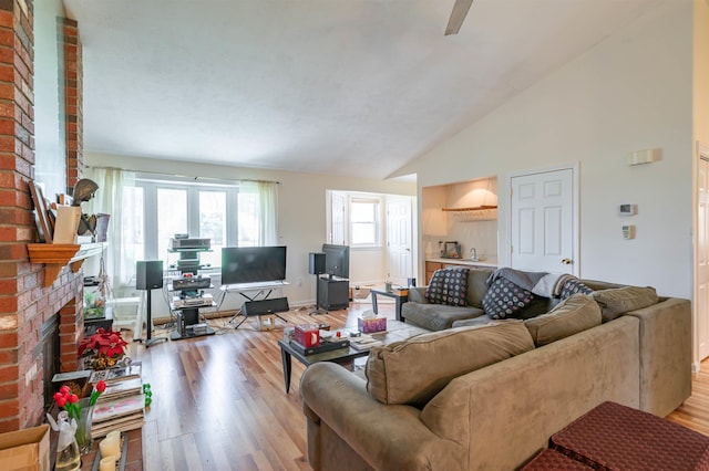 living area featuring baseboards, a fireplace, vaulted ceiling, and light wood-style flooring
