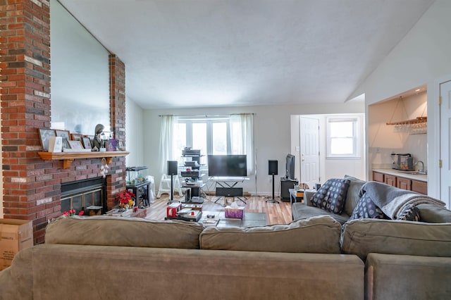 living area featuring wood finished floors, vaulted ceiling, a brick fireplace, and a wealth of natural light