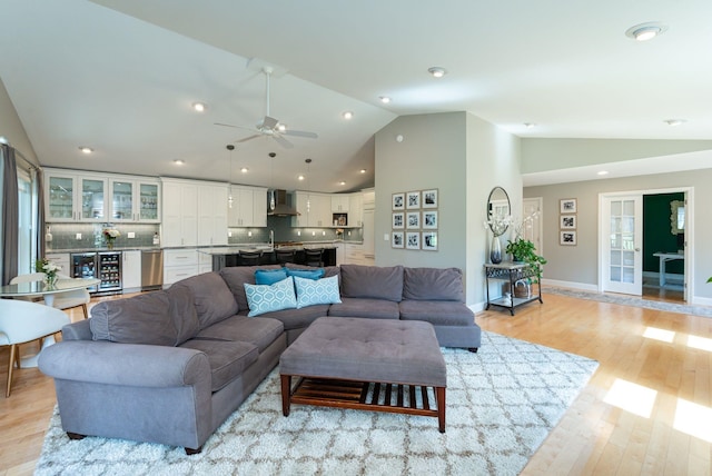 living room with beverage cooler, baseboards, light wood-type flooring, a ceiling fan, and vaulted ceiling