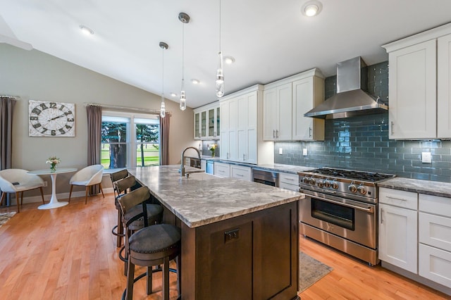 kitchen with lofted ceiling, stainless steel stove, wall chimney range hood, a sink, and backsplash