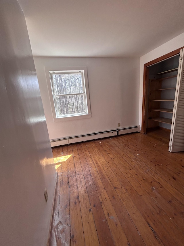 unfurnished bedroom featuring a baseboard heating unit and hardwood / wood-style flooring