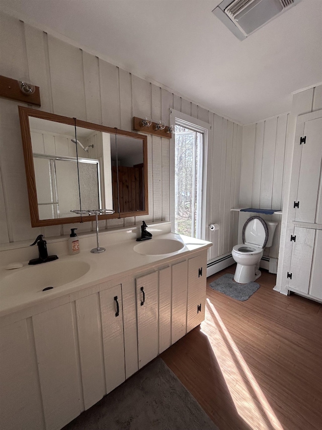 full bathroom featuring a sink, a baseboard heating unit, wood finished floors, and toilet