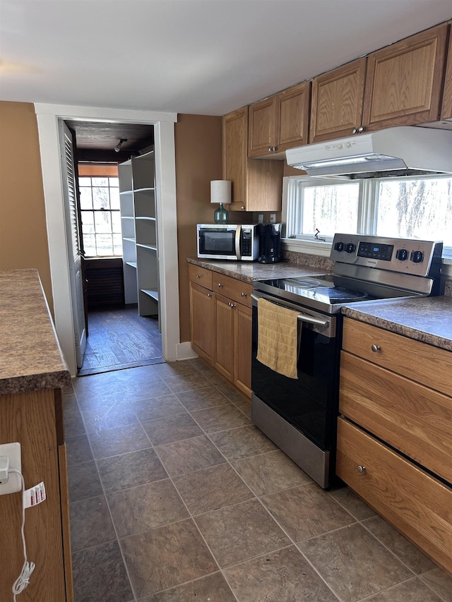 kitchen with ventilation hood, appliances with stainless steel finishes, brown cabinets, and dark countertops
