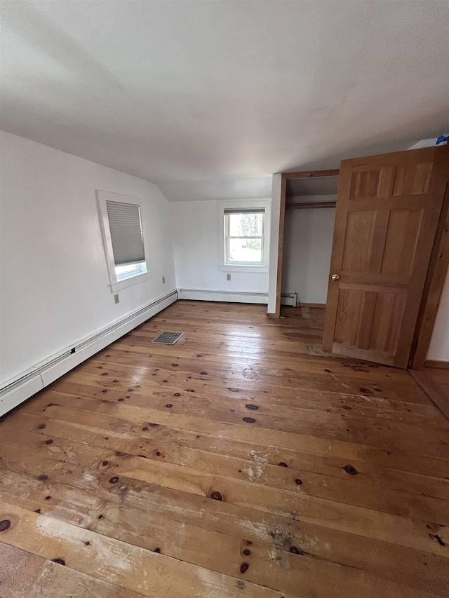 unfurnished bedroom with wood-type flooring, visible vents, a closet, baseboards, and baseboard heating