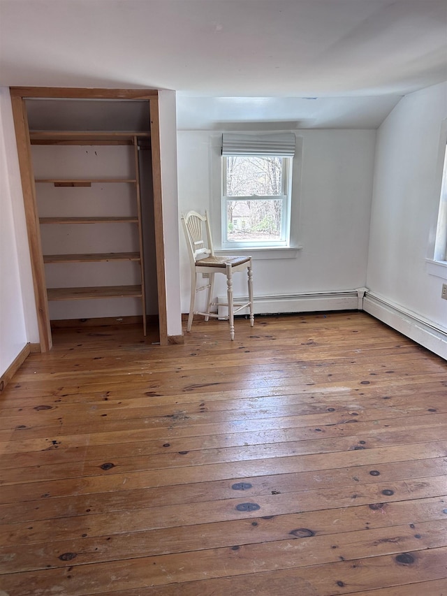 unfurnished bedroom with wood-type flooring and a baseboard heating unit