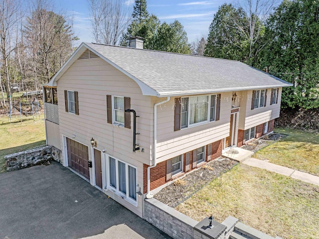 bi-level home featuring roof with shingles, an attached garage, a front lawn, aphalt driveway, and a chimney