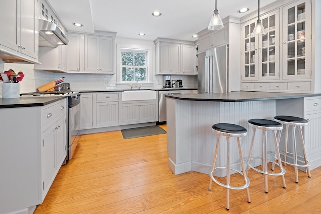 kitchen featuring a sink, wall chimney range hood, a kitchen bar, dark countertops, and appliances with stainless steel finishes