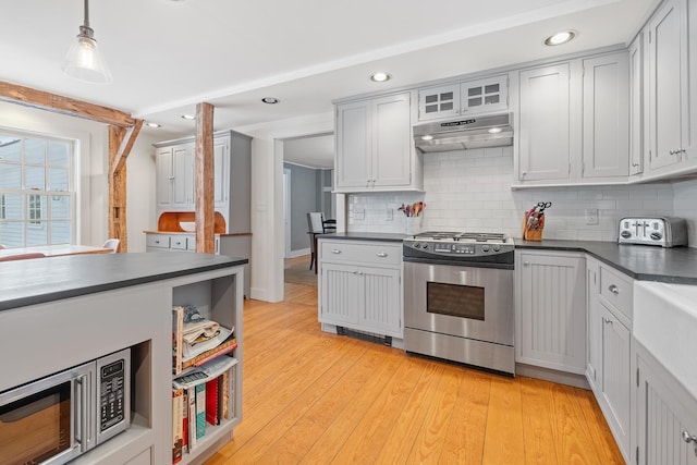 kitchen featuring under cabinet range hood, dark countertops, stainless steel appliances, and tasteful backsplash