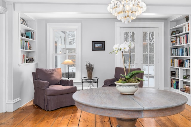 living area with built in shelves, hardwood / wood-style floors, and a notable chandelier