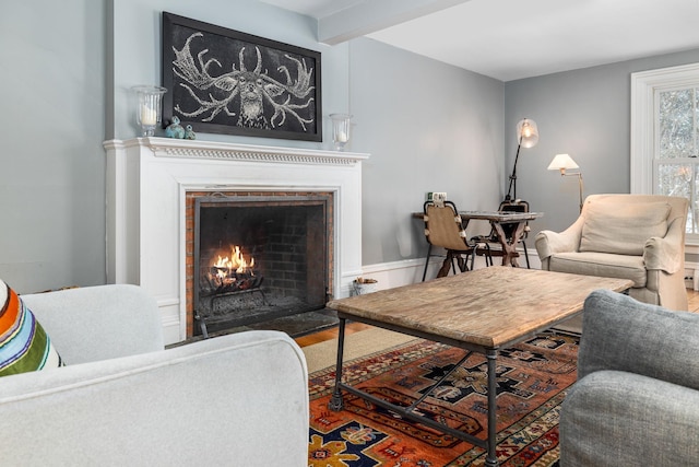 living room with a warm lit fireplace, beam ceiling, and wood finished floors