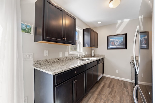 interior space with baseboards, dark wood-type flooring, light stone counters, a sink, and appliances with stainless steel finishes