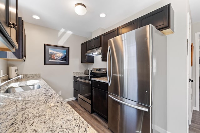 kitchen with dark wood-style flooring, appliances with stainless steel finishes, a sink, light stone counters, and under cabinet range hood