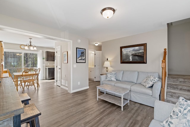 living room featuring an inviting chandelier, baseboards, stairway, and wood finished floors