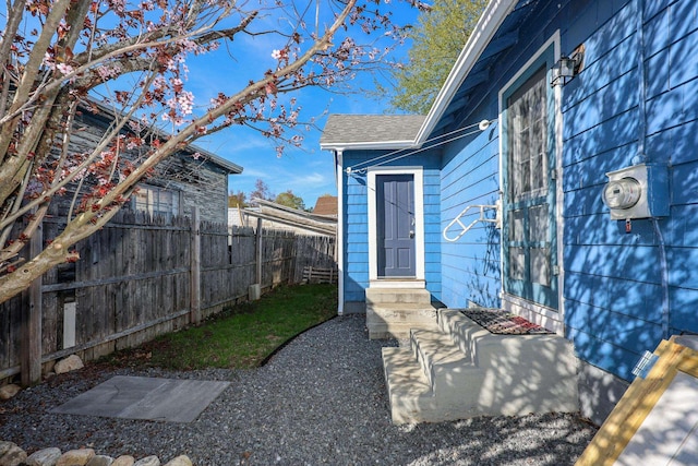 doorway to property featuring fence and roof with shingles