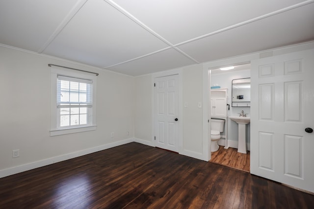 unfurnished bedroom featuring baseboards, ensuite bathroom, and dark wood-style floors