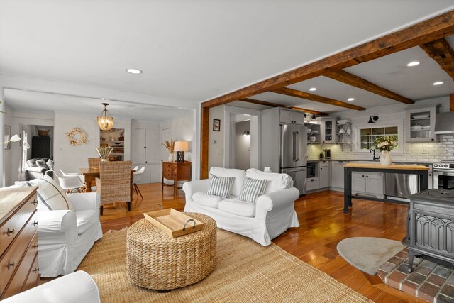living area featuring wood-type flooring, recessed lighting, beamed ceiling, and a wood stove