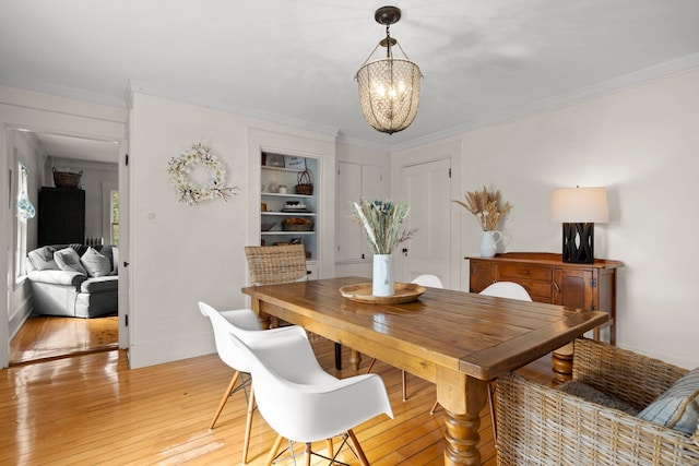 dining area with light wood-style floors, crown molding, a chandelier, and built in shelves