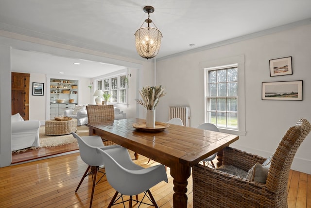 dining area with ornamental molding, light wood finished floors, a chandelier, and built in shelves