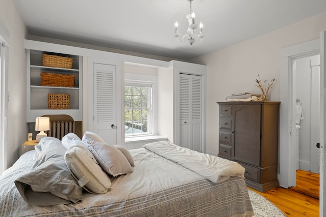 bedroom with an inviting chandelier, light wood-style floors, and multiple closets
