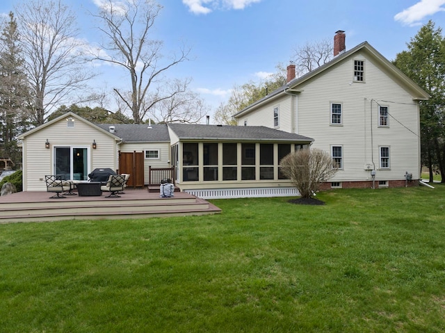 rear view of property featuring a lawn, a deck, a chimney, and a sunroom