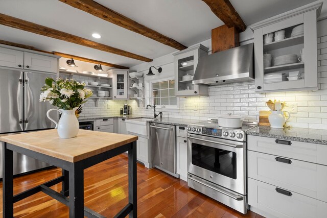 kitchen featuring light stone countertops, dark wood-type flooring, wall chimney exhaust hood, a sink, and appliances with stainless steel finishes
