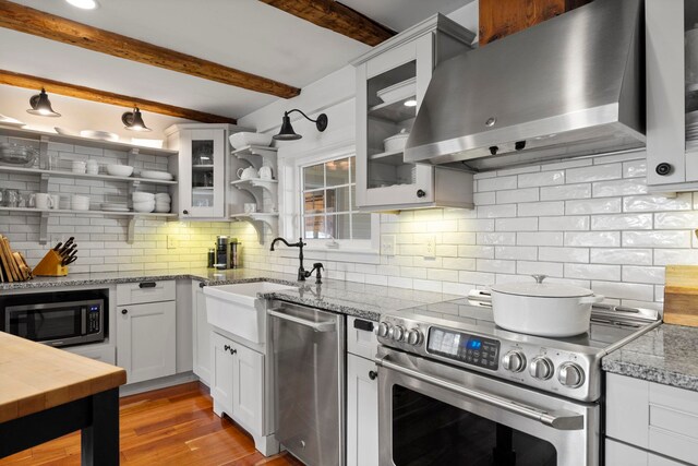 kitchen with wall chimney range hood, open shelves, appliances with stainless steel finishes, a sink, and tasteful backsplash