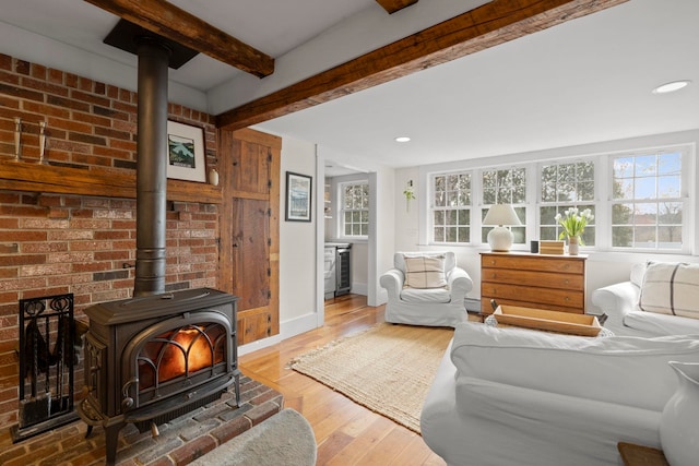 living area featuring wood finished floors, a wood stove, baseboards, and beam ceiling