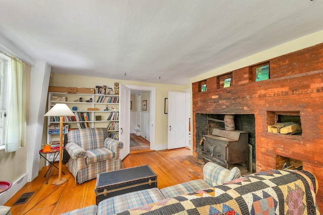 living room featuring wood-type flooring, a wood stove, baseboards, and visible vents