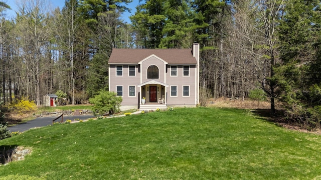 colonial home with a wooded view, a chimney, and a front lawn