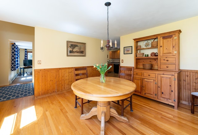 dining area featuring wooden walls, a wainscoted wall, and light wood finished floors