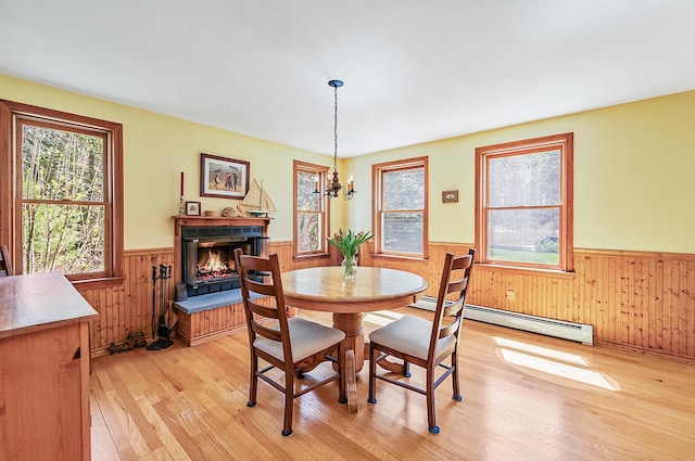 dining area with wooden walls, a wainscoted wall, light wood-type flooring, and a healthy amount of sunlight