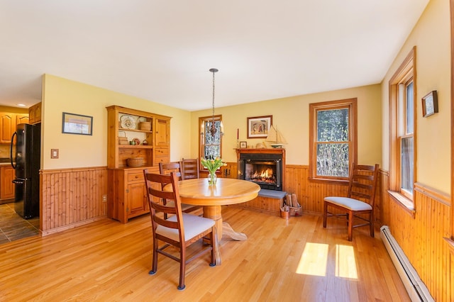 dining space featuring wooden walls, baseboard heating, and wainscoting