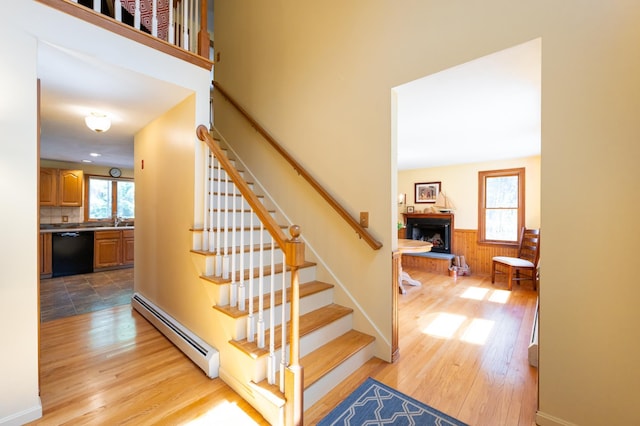 staircase featuring a fireplace with raised hearth, a baseboard heating unit, wood finished floors, and a wealth of natural light