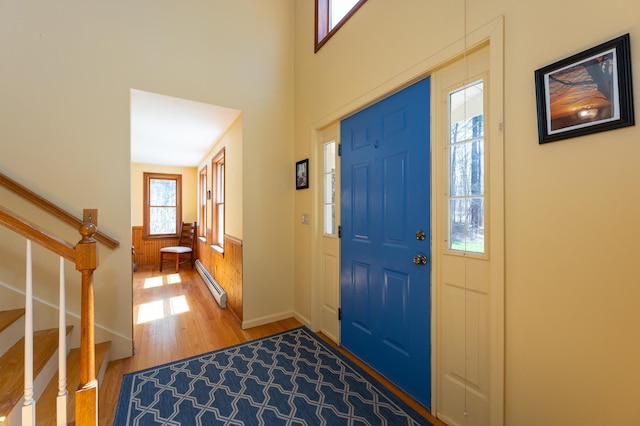 foyer entrance with stairs, a baseboard heating unit, wainscoting, and wood finished floors