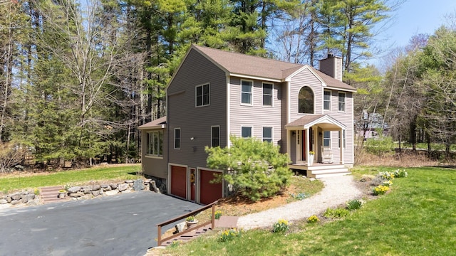 colonial inspired home with an attached garage, driveway, a chimney, and a front yard