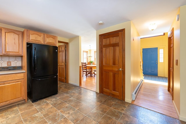 kitchen with freestanding refrigerator, baseboards, baseboard heating, stone finish floor, and backsplash