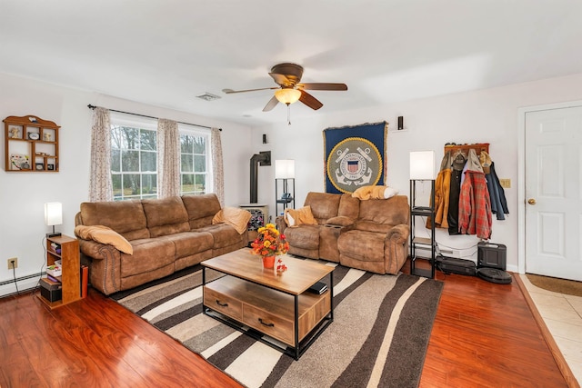 living area with a ceiling fan, visible vents, wood finished floors, baseboards, and a baseboard radiator