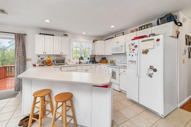 kitchen with a kitchen breakfast bar, white cabinetry, a peninsula, white appliances, and light tile patterned flooring